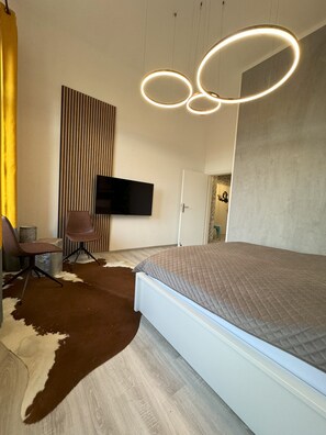 A modern bedroom with a large bed, a mounted TV, and a unique circular light fixture. - Görlitz - Design Apartment Iii, Hell, 35qm Zkb, Zentral zu Grenze Altstadt Park (Görlitz)