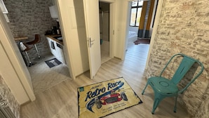 Un couloir avec un coin cuisine, une porte donnant sur une autre pièce et un fauteuil de couleur turquoise.
