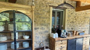 A rustic kitchen with wooden shelves and a stone wall, a coffee machine, and a wicker basket. - Chambres et Table D'hôte au Cœur de la Castagniccia Dans une Bâtisse du Xviii S (Verdèse)