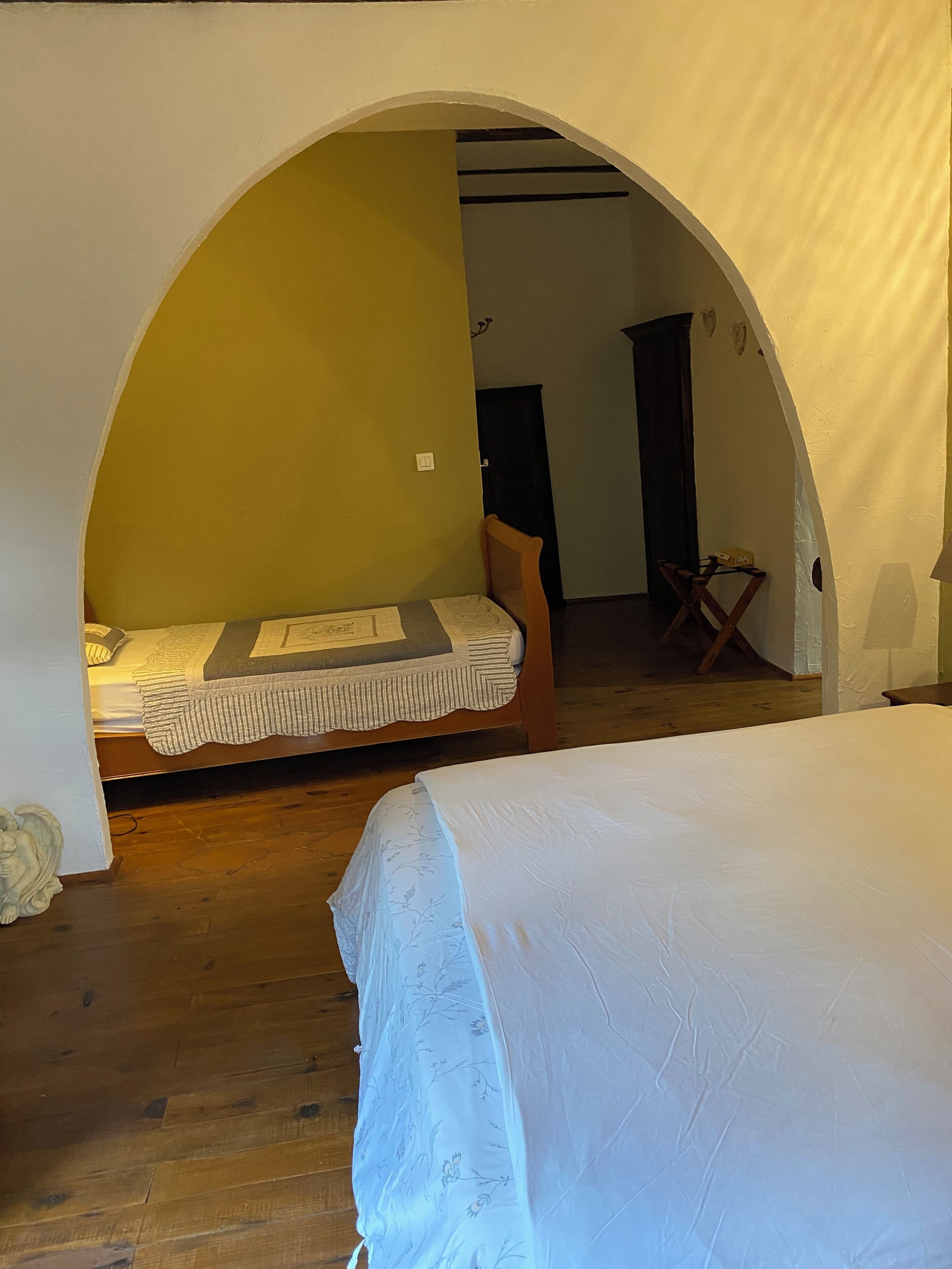Een slaapkamer met twee bedden, houten vloeren en een rondboogvormige deur naar een andere kamer.