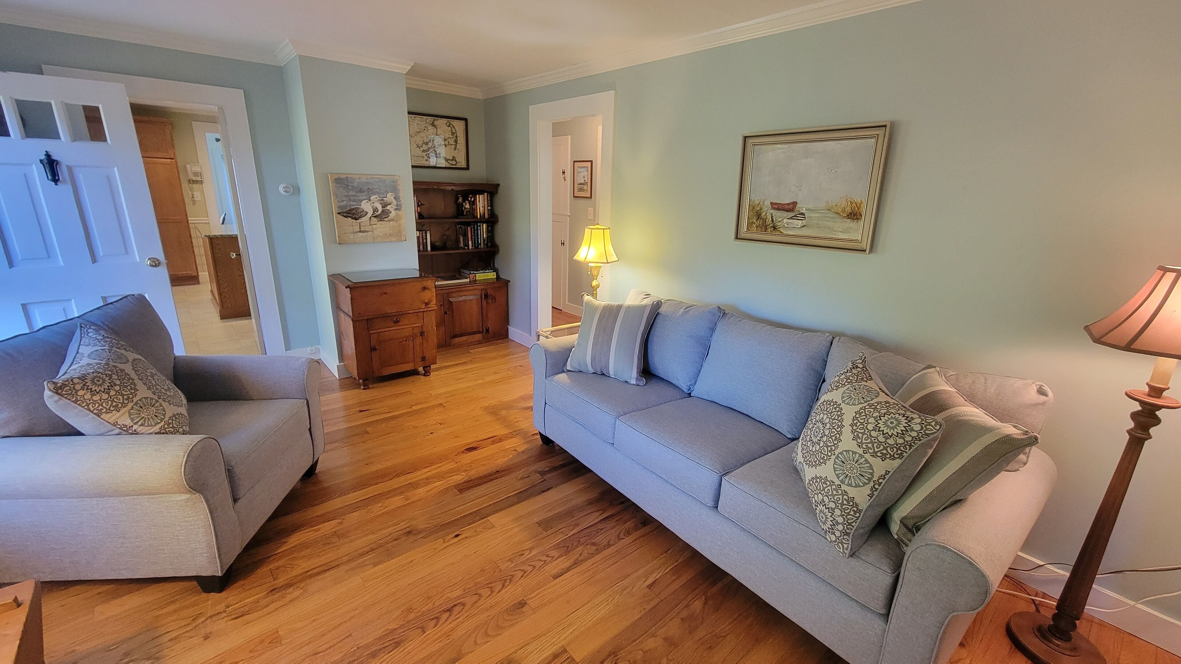 A living room with a sofa, armchairs, wooden flooring, and a lamp.