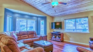 A spacious living room with a large leather sofa, a television, and a ceiling fan. - Buttercup Haven at Pine Mountain Lake (Groveland)