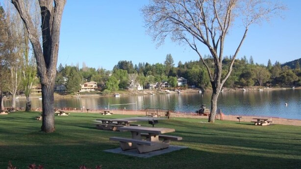 A lakeside park with picnic tables and a view of a lake and houses in the background. - Buttercup Haven at Pine Mountain Lake (Groveland)