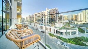 A balcony with wicker furniture overlooking a modern urban area with high-rise buildings and a road. - Ravishing 2BR at Azizi Riviera 30, Al Merkadh by Deluxe Holiday Homes (Dubai)