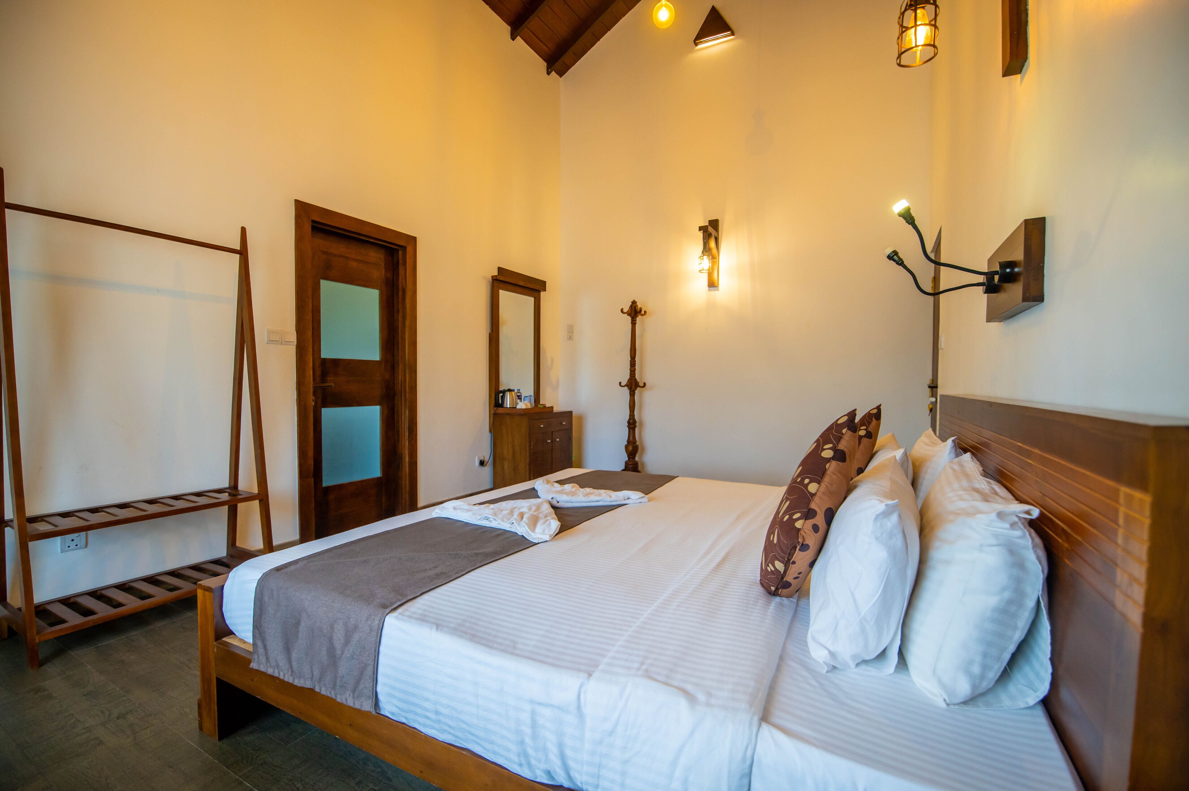 A neatly made bed with pillows and a blanket, a wooden headboard, a wooden wardrobe, a mirror, and wall-mounted lights.