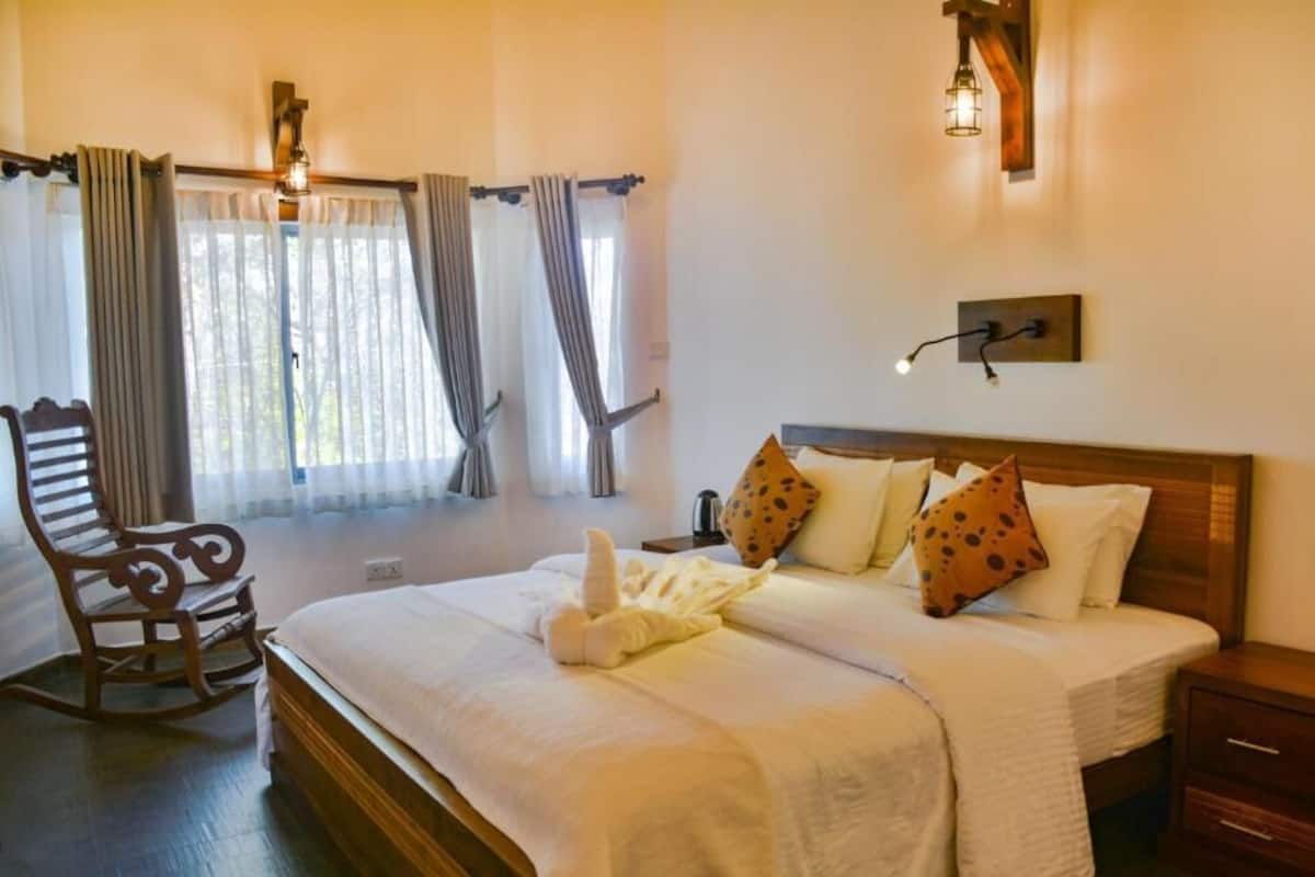 A neatly made bed with pillows and a blanket, a wooden rocking chair, and a bedside table with a lamp.