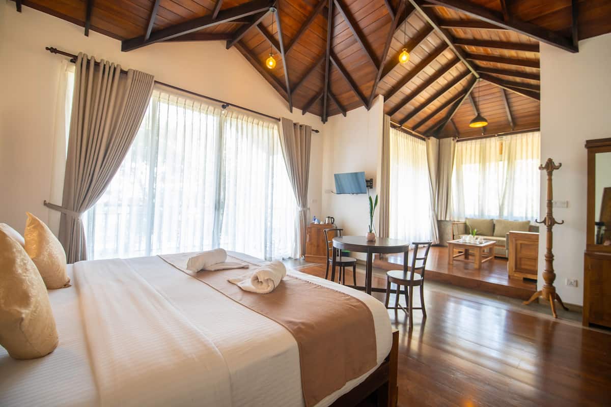 A hotel room with a large bed, wooden ceiling, and a dining area with a table and chairs.