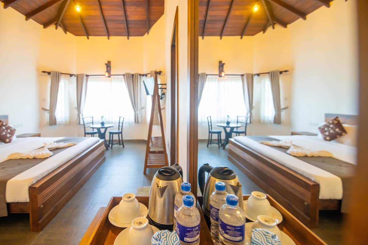 A hotel room with a wooden bed, a bench, a table with tea set, and a mirror reflecting the room.