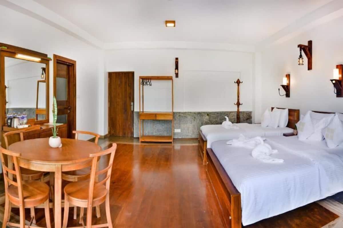 A hotel room with a wooden dining table, two beds, a mirror, and wall-mounted lights.