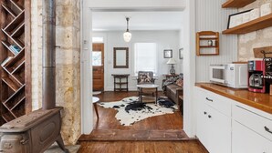 A cozy kitchen with a stove, microwave, and shelves. A cowhide rug is on the floor, and there's a wooden chair. - Newly Renovated | 2BR | Hot Tub | Walk to Downtown (Fredericksburg)