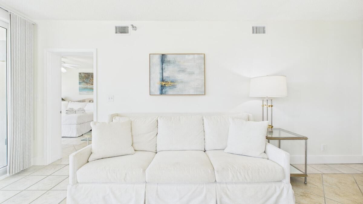 Un salón blanco con un sofá blanco, una mesita de cristal y un cuadro abstracto enmarcado en la pared.