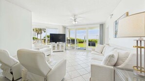 A spacious living room with a large TV, white furniture, and a balcony with a view. - Tranquil Paradise 120-Gulf Views-Sleeps 6 (Alys Beach)