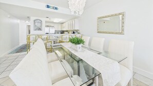 A modern dining area with a glass table, white chairs, and a central plant. - Tranquil Paradise 120-Gulf Views-Sleeps 6 (Alys Beach)