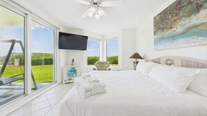 A bedroom with a large bed, a television, a chair, and a view of the outdoors. - Tranquil Paradise 120-Gulf Views-Sleeps 6 (Alys Beach)