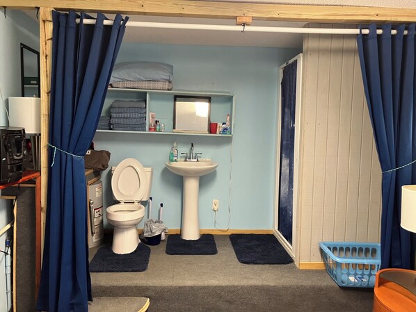 A compact bathroom with a toilet, sink, and shelves with toiletries.