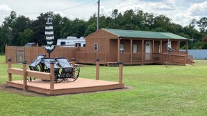 A wooden deck with outdoor furniture, a small building with a green roof, and a fenced area. - Quiet Cabin with Owa theme park, shopping, dining and the beach minutes away.  (Elberta)