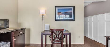 A hotel room with a kitchenette, a dining table with a chair, a framed picture on the wall, and a carpeted floor.