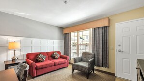 Una sala de estar con un sofá rojo, un sillón estampado y una lámpara.