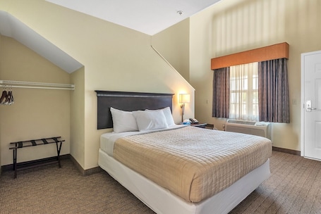 A hotel room with a bed, a bedside table with a lamp, a coat rack, and a window with curtains.