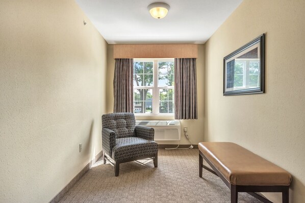 A hotel room with a patterned armchair, a bench, a radiator, and a window with curtains.