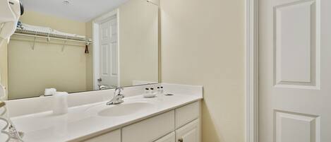 A bathroom with a white sink, mirror, and vanity with drawers. There are lights above the mirror and a towel rack above the sink.