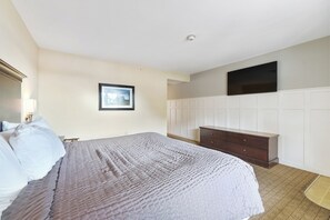 Ein Schlafzimmer mit einem Bett, einem Schminktisch, einem flachbildfernseher an der Wand und einem gerahmten Bild.