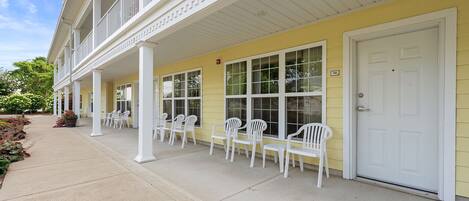 A building with a yellow exterior, white columns, and a covered porch with white plastic chairs.