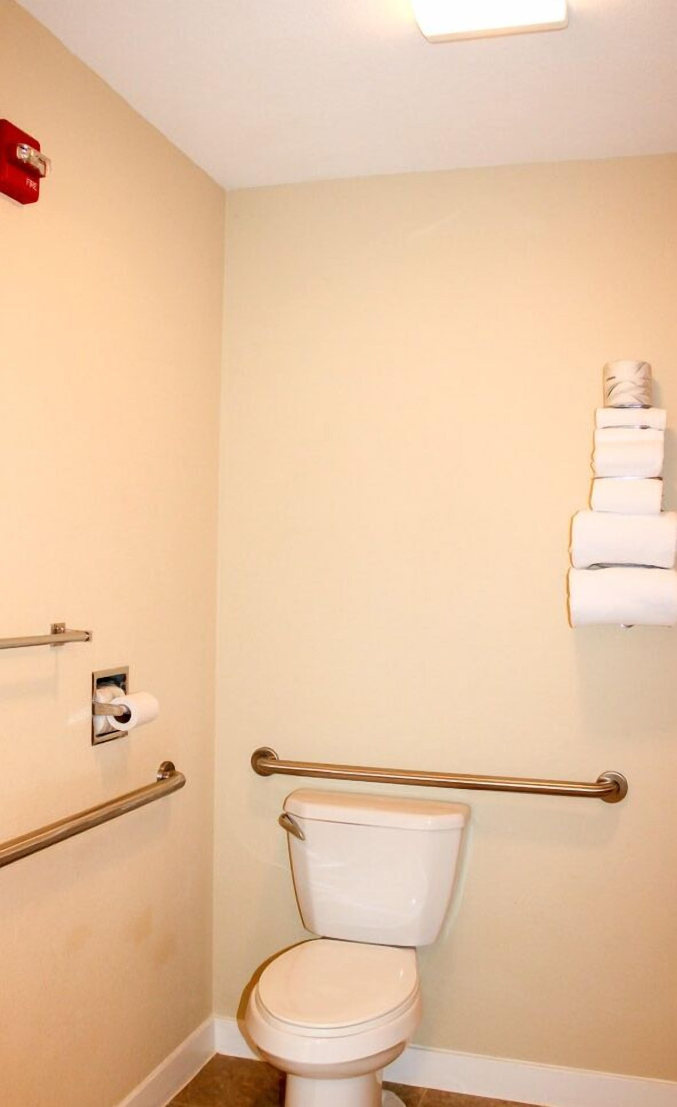Een badkamer met een toilet, een handgreep, een toiletrolhouder en een handdoekdispenser.