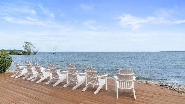 A wooden deck with white Adirondack chairs facing a calm body of water. - ADA Glacier Suite at Kelley's Island Venture Resort (Kelleys Island)