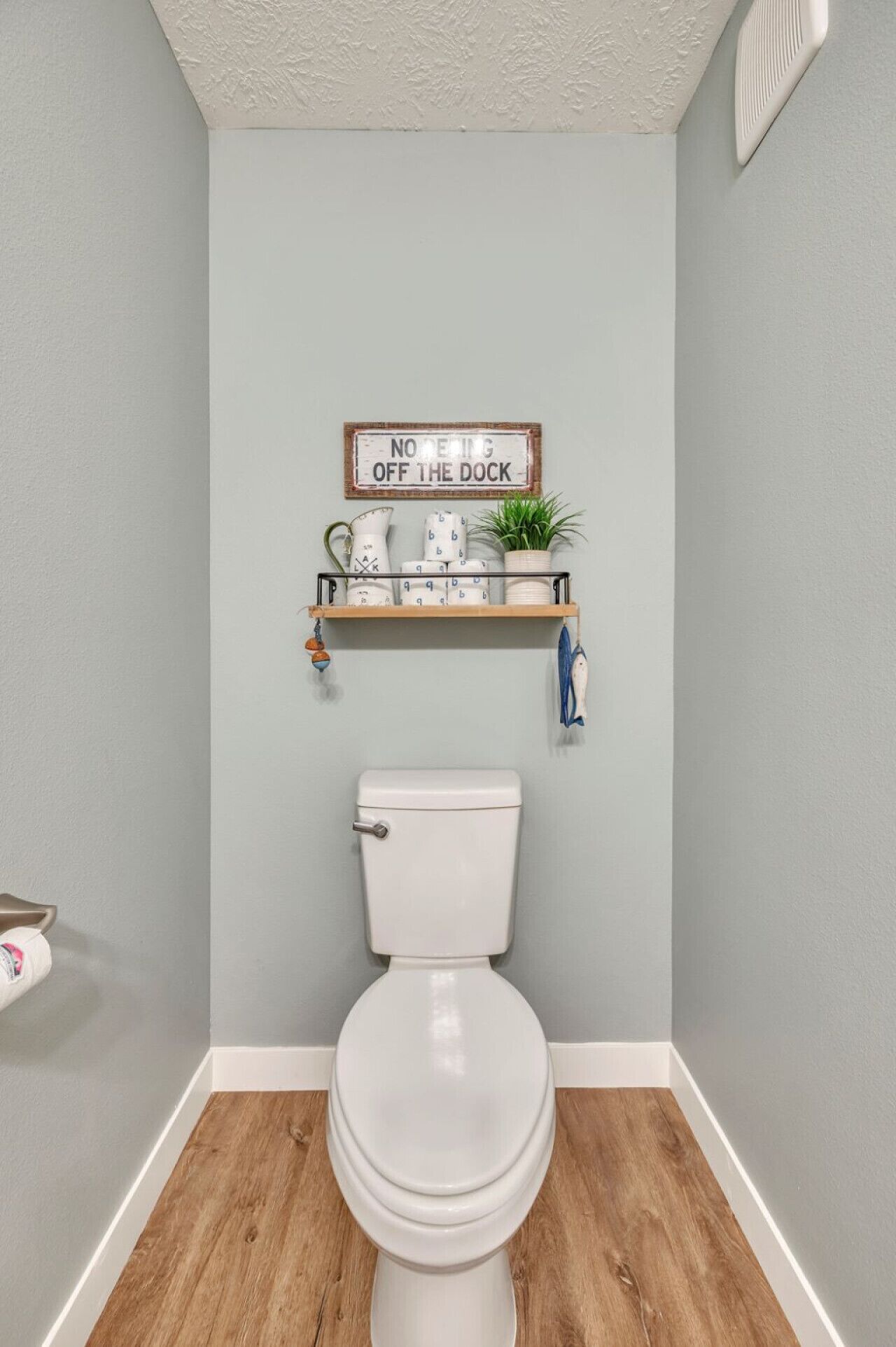 Un baño con inodoro, una repisa con adornos y un cartel sobre el inodoro.