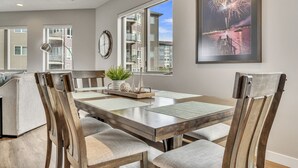 A dining area with a wooden table, cushioned chairs, a clock, and a framed picture of fireworks.