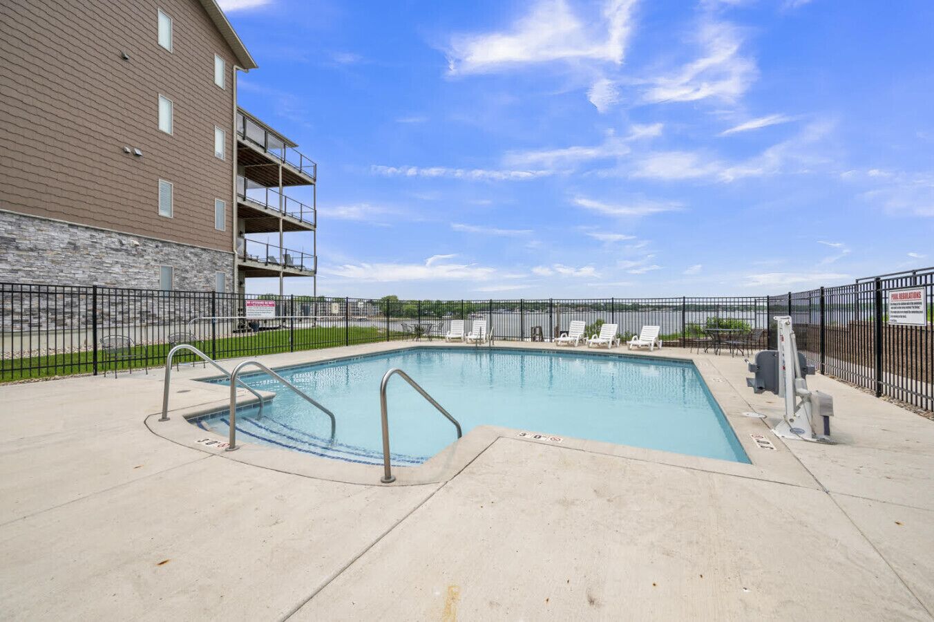 A rectangular swimming pool with a concrete deck, surrounded by a black metal fence.