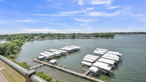 A marina with multiple docked boats, a wooden pier, and a backdrop of trees and buildings.