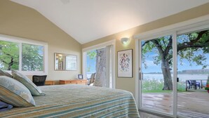 A bedroom with a large bed, a desk, and a chair. There are windows with a view of trees and a deck outside. - The Lakeside Lookout on East Lake`s Gingles Point (Arnolds Park)