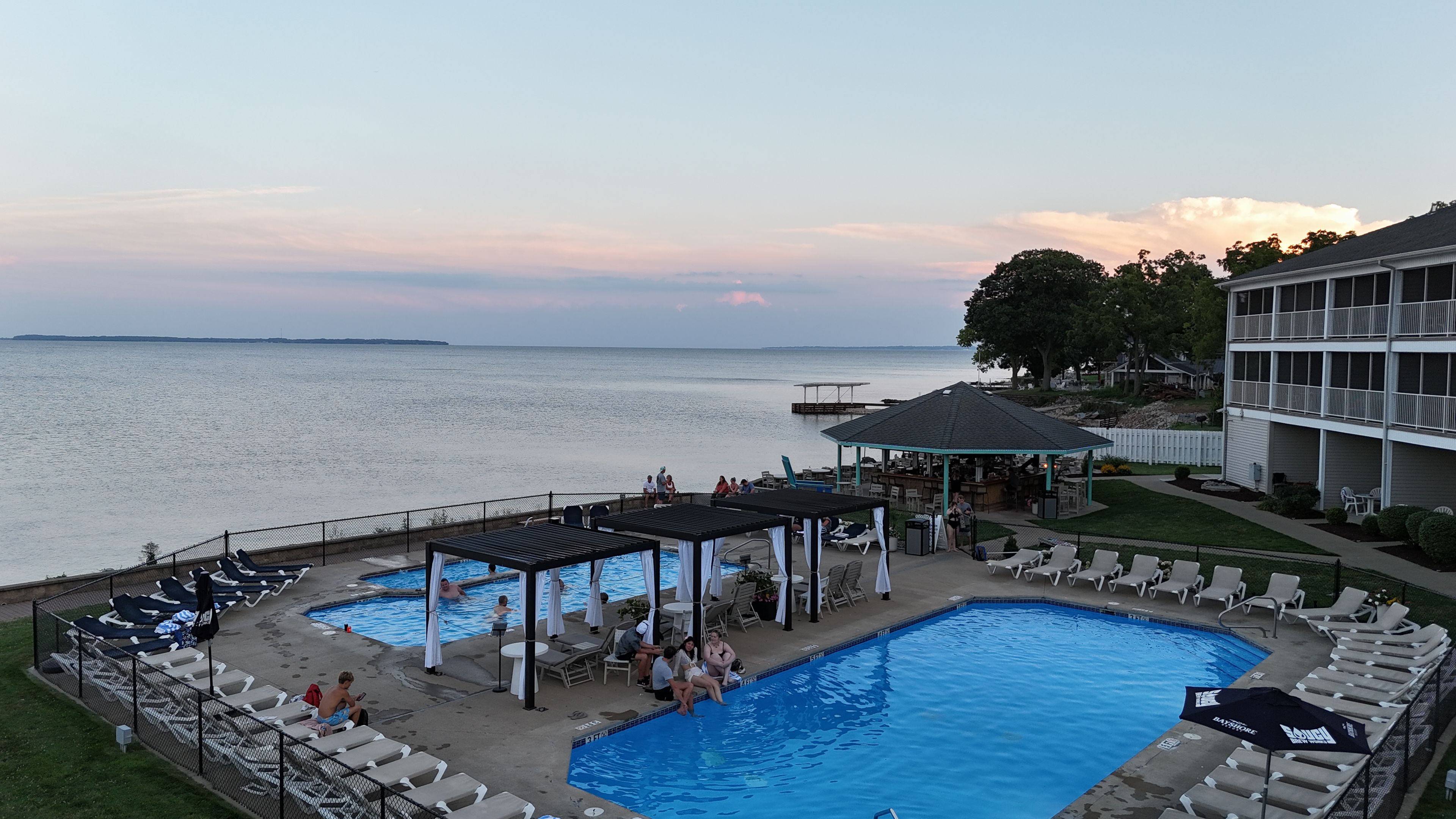 A pool area with lounge chairs and umbrellas, a bar, and a view of the water.