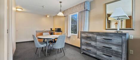 A hotel room with a dining area, a large mirror, and a dresser.
