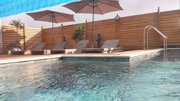 A swimming pool with lounge chairs and umbrellas, wooden deck, and a wooden fence. - Ô Licuala Villa (Petite Île)
