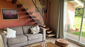 A living room with a sofa, a coffee table, a patterned rug, a hanging chair, and a staircase.