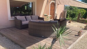 A covered outdoor seating area with wicker furniture, a wooden deck, and potted plants.