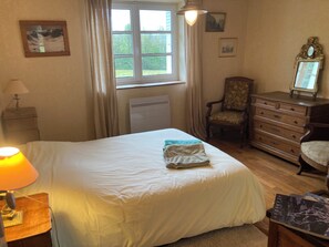 Um quarto com uma cama, uma cadeira, uma cômoda e uma janela com cortinas.