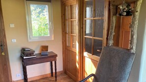 A room with a wooden chair, a table with books and a radio, a window with blinds, and a door with a key hanging on it.