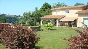 A house with a covered patio, a lawn, and surrounding greenery.