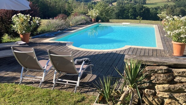 A swimming pool with a wooden deck, two lounge chairs, and potted plants.