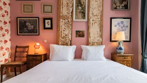 A neatly arranged bedroom with a large bed, two bedside tables, a chair, and floral wallpaper.