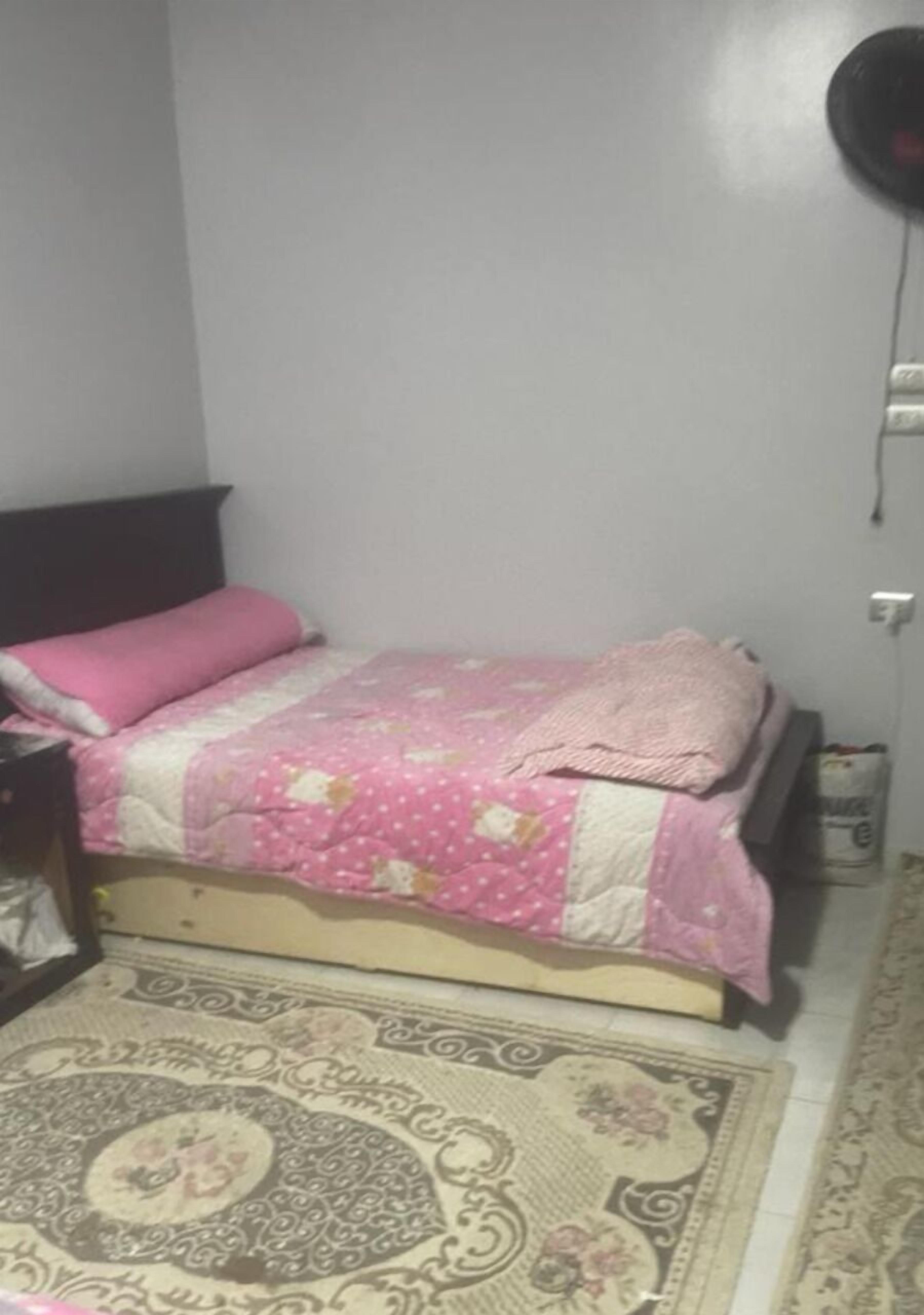 Ein kleines, aufgeräumtes Schlafzimmer mit Bett, Nachttisch, Teppich und einer Steckdose.