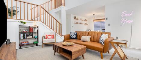 A modern living room with a staircase, a sofa, a coffee table, and a neon sign.