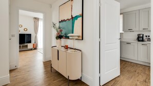 A modern kitchen with white cabinets, a dining area with a table and chairs, and a hallway leading to another room. - Tranquil 4-Bed Oasis Modern & Chic (Oxford)