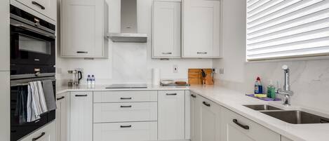 A modern kitchen with white cabinetry, a built-in oven, and a stainless steel range hood.