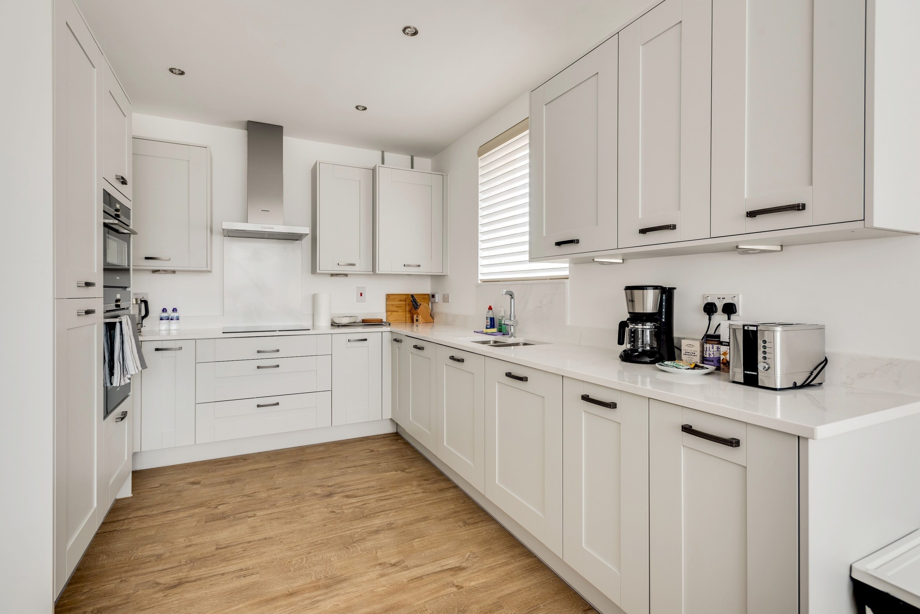 A modern kitchen with white cabinetry, a wooden floor, and a built-in oven.