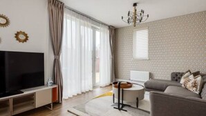 A modern living room with a flat-screen TV, a grey sofa, a small round table, and a chandelier. - Tranquil 4-Bed Oasis Modern & Chic (Oxford)